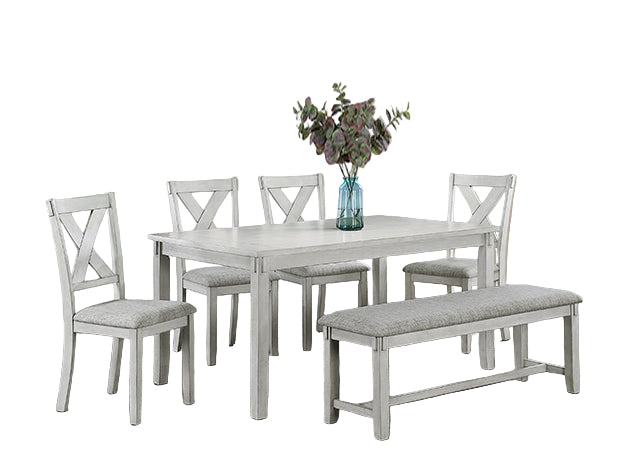 Dining room set with white table and chairs on a gray rug, featuring a vase with flowers.