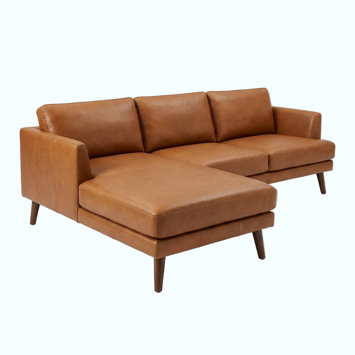 A mid-century modern sectional sofa in warm cognac brown leather, featuring a right-facing chaise lounge and tapered dark wood legs, photographed on a light gray studio background.