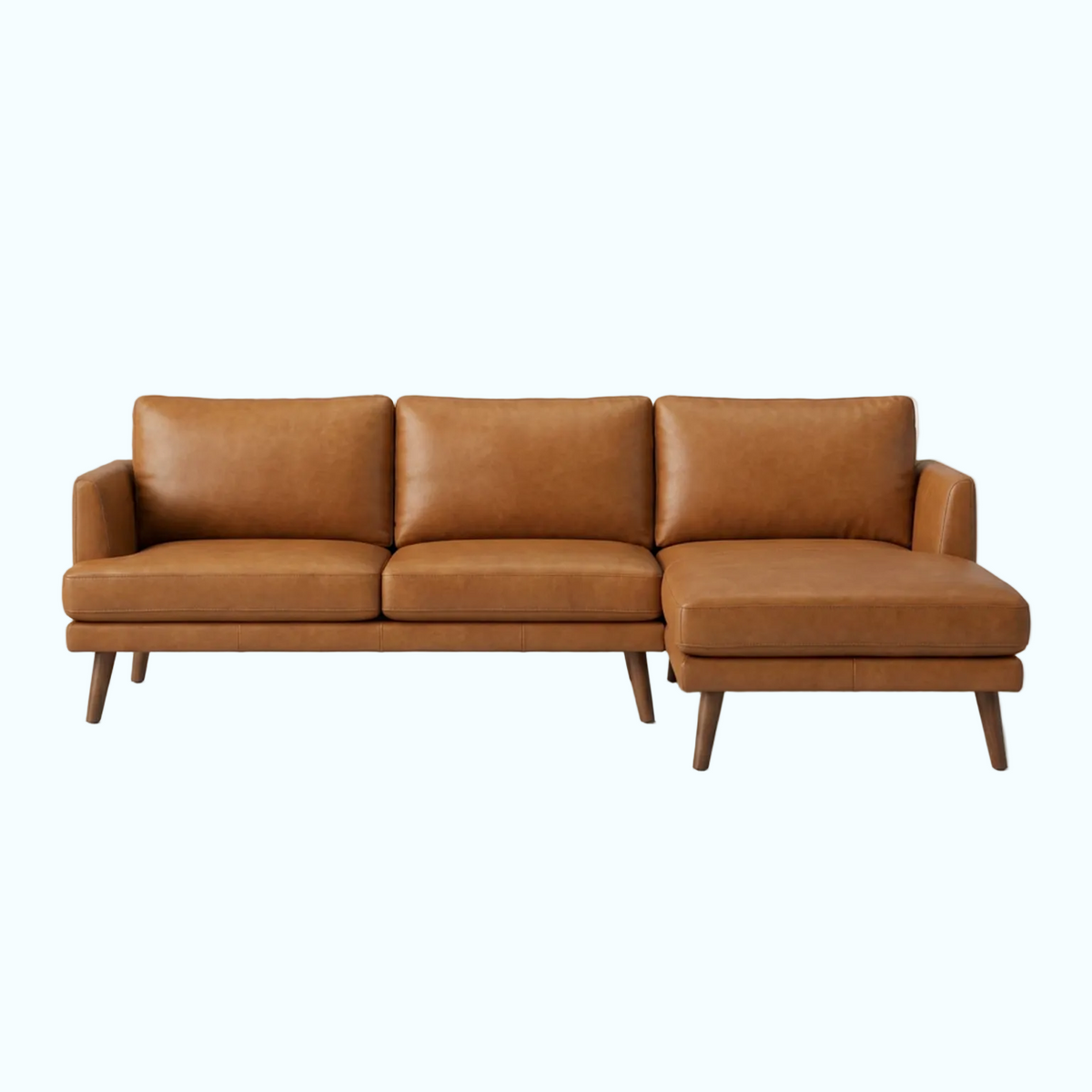 A mid-century modern three-seat sofa with a right-side chaise lounge, upholstered in warm tan leather with tapered dark wood legs, shown against a plain light gray studio background.