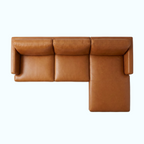 A top-down view of a modern sectional sofa in warm tan leather, featuring a three-seat cushion, a right-side armrest, and a right-side chaise lounge, set against a solid light gray background.