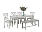 Dining room set with white table and chairs on a gray rug, featuring a vase with flowers.