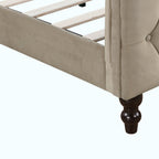 Close-up of a tufted upholstered bed frame with a beige velvet headboard, wooden slats, and black turned legs on a white background.