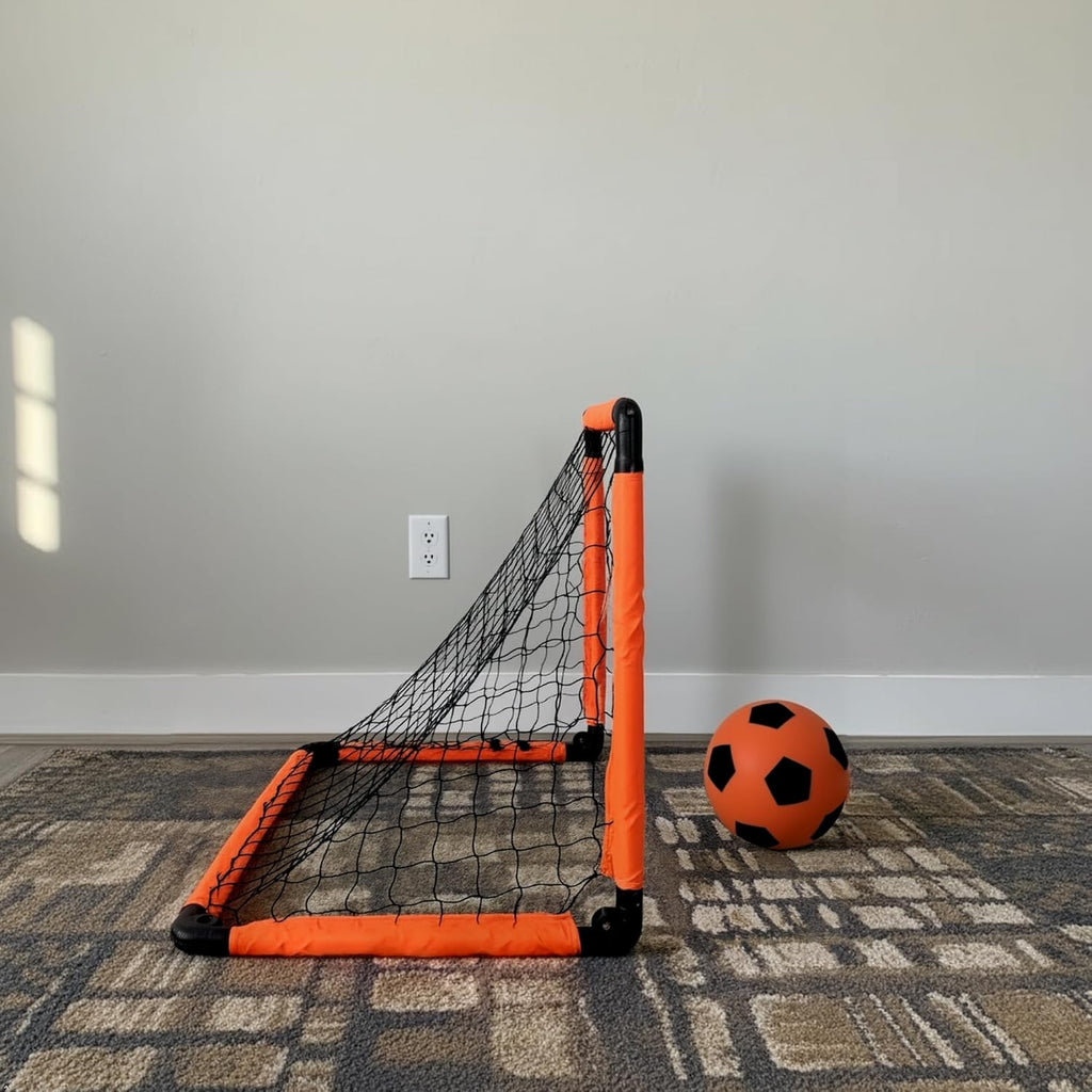 Mini soccer goal with orange frame and black net on a carpeted floor against a gray wall.