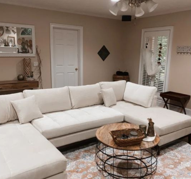 A large cream-colored sectional sofa in a cozy living room setting, paired with a round wooden coffee table and a patterned rug.
