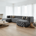 Gray tufted sectional sofa in a modern living room with large windows.
