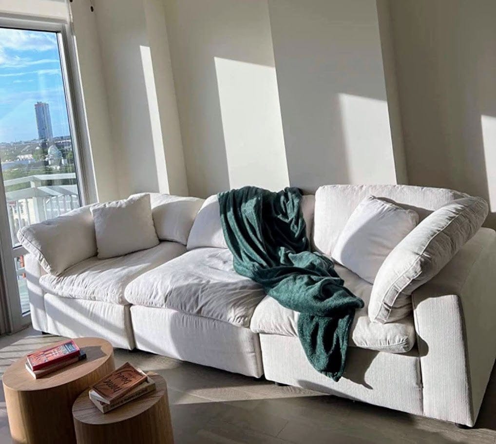 White sectional sofa with a green blanket in a room with large windows.