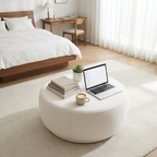 Modern bedroom with a laptop on a round white table, books, and a cup of coffee.