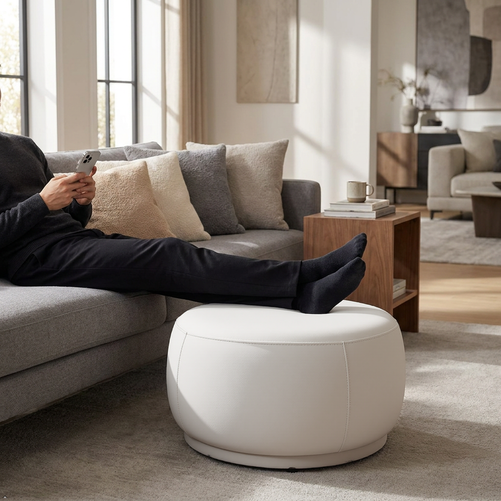 Person relaxing on a couch with feet up on a white ottoman in a modern living room.