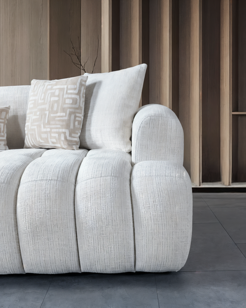 White textured sofa with patterned cushions against a wooden paneled wall.