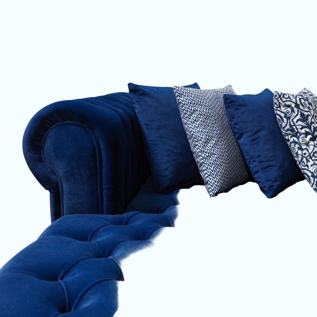 Blue tufted sofa with decorative pillows on a white background