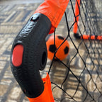 Close-up of a black and orange goalpost with a ball in the background on a textured surface.