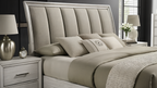 Beige upholstered bed with matching nightstands and lamps in a bedroom setting.