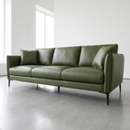 An olive green leather three-seater sofa with matching throw pillows, supported by slim black metal legs, set in a minimalist modern room with a concrete floor and white walls.