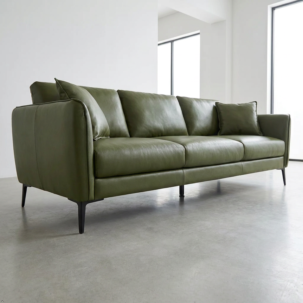 An olive green leather three-seater sofa with black tapered legs, shown in a minimalist modern room with concrete floors and white walls.