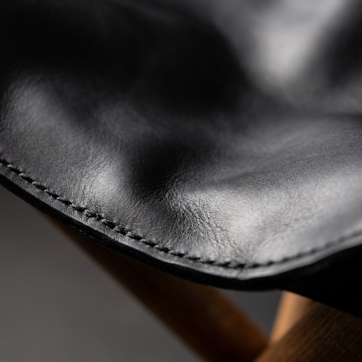 Close-up of a black leather seat or cushion with visible stitching and a wooden support edge in the background.