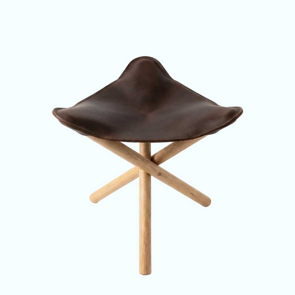 A modern stool with a dark brown leather seat and a light natural wood X-frame base, photographed on a seamless white background.