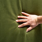 A close-up of a hand pressing into a dark olive green fabric surface to show its texture and elasticity.