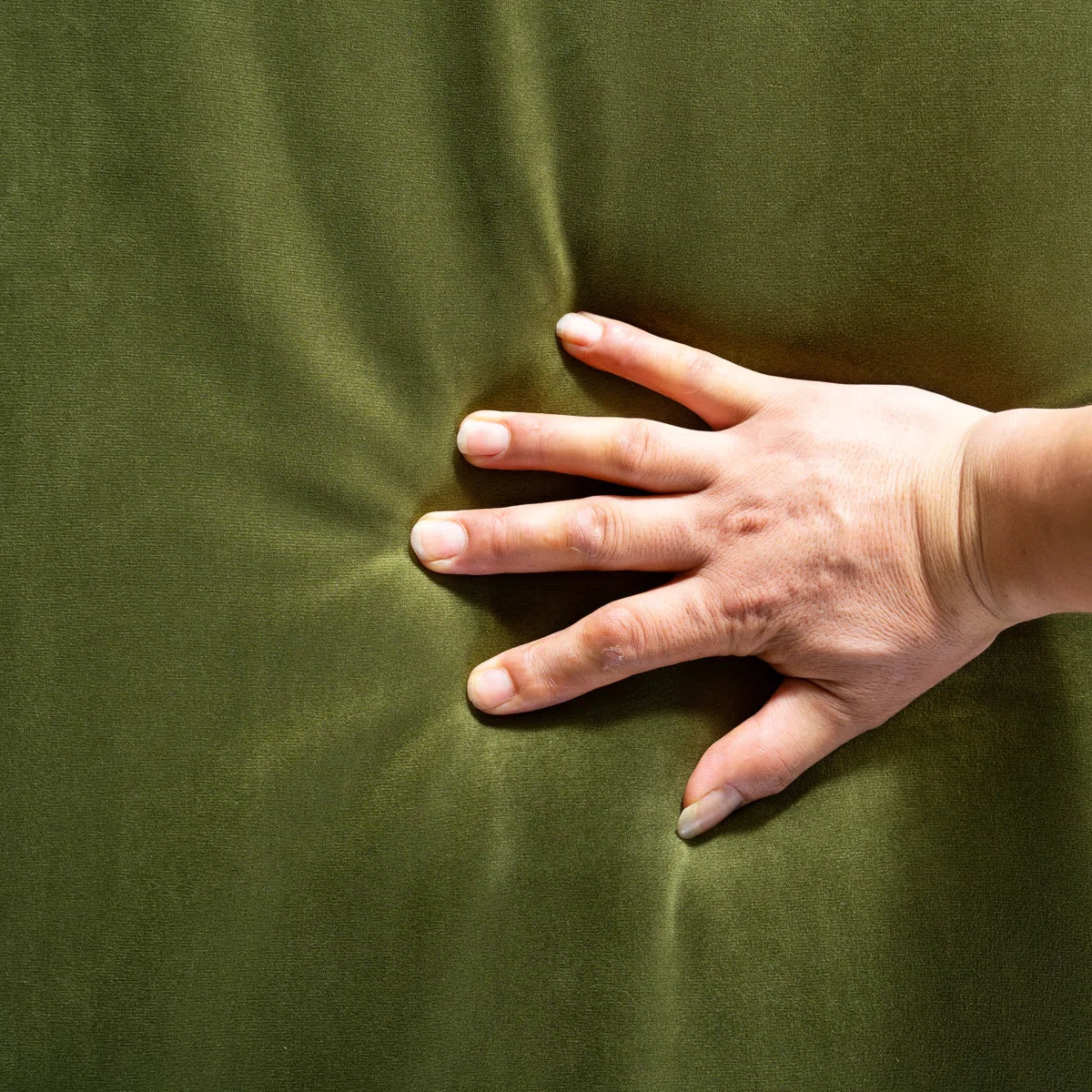 A close-up of a hand pressing into a dark olive green fabric surface to show its texture and elasticity.