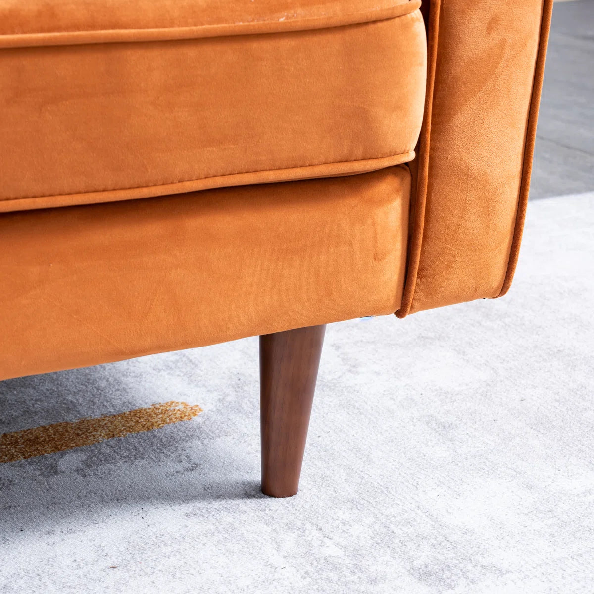 Close-up of an orange upholstered chair corner with a tapered dark wood leg on a light gray rug.