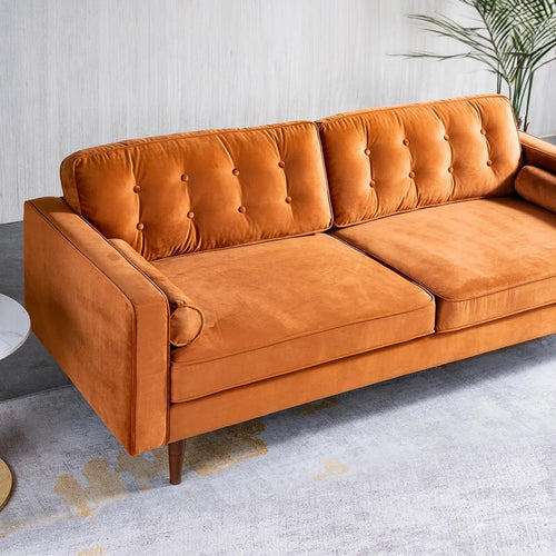 An orange velvet sofa with tufted back cushions and wooden legs, shown in a modern living room setting with a gray rug and a potted plant.