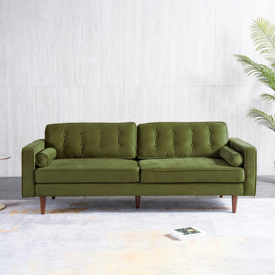 An olive green tufted velvet loveseat sofa with tapered wooden legs, positioned against a light gray textured wall with a potted palm in the background.
