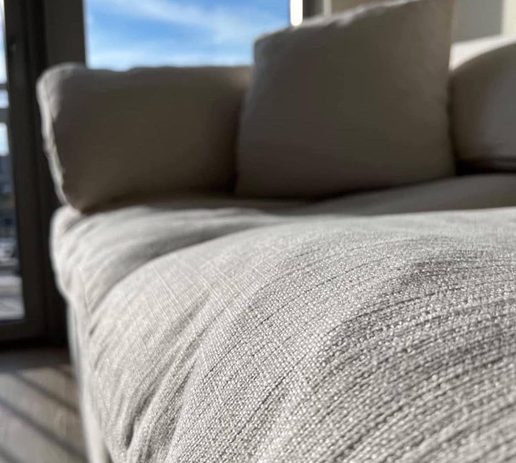 Close-up of a textured gray fabric surface with pillows in the background