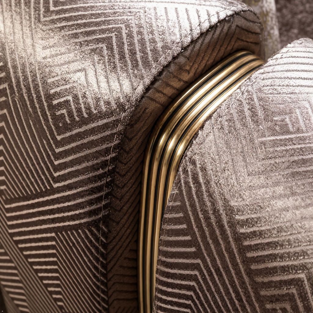 Close-up of upholstered furniture showing a metallic taupe fabric with a geometric line pattern and a curved gold metal trim accent.