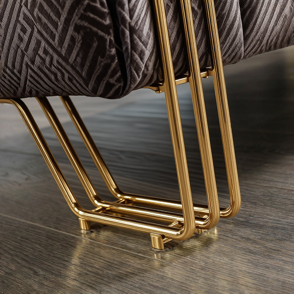 Close-up of a modern chair or stool with a dark gray patterned fabric seat and polished gold metal legs on a wood floor.