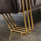 Close-up of a modern chair or stool with a dark gray patterned fabric seat and polished gold metal legs on a wood floor.