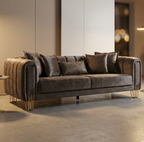 A modern gray velvet sofa with gold metal legs and matching throw pillows, styled in a contemporary minimalist living room setting.