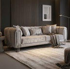 A modern gray velvet sofa with matching throw pillows and a draped knit blanket, set in a contemporary living room with a slatted wood accent wall, a side table, and a striped area rug.
