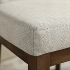 Close-up of a textured fabric chair seat with wooden legs.