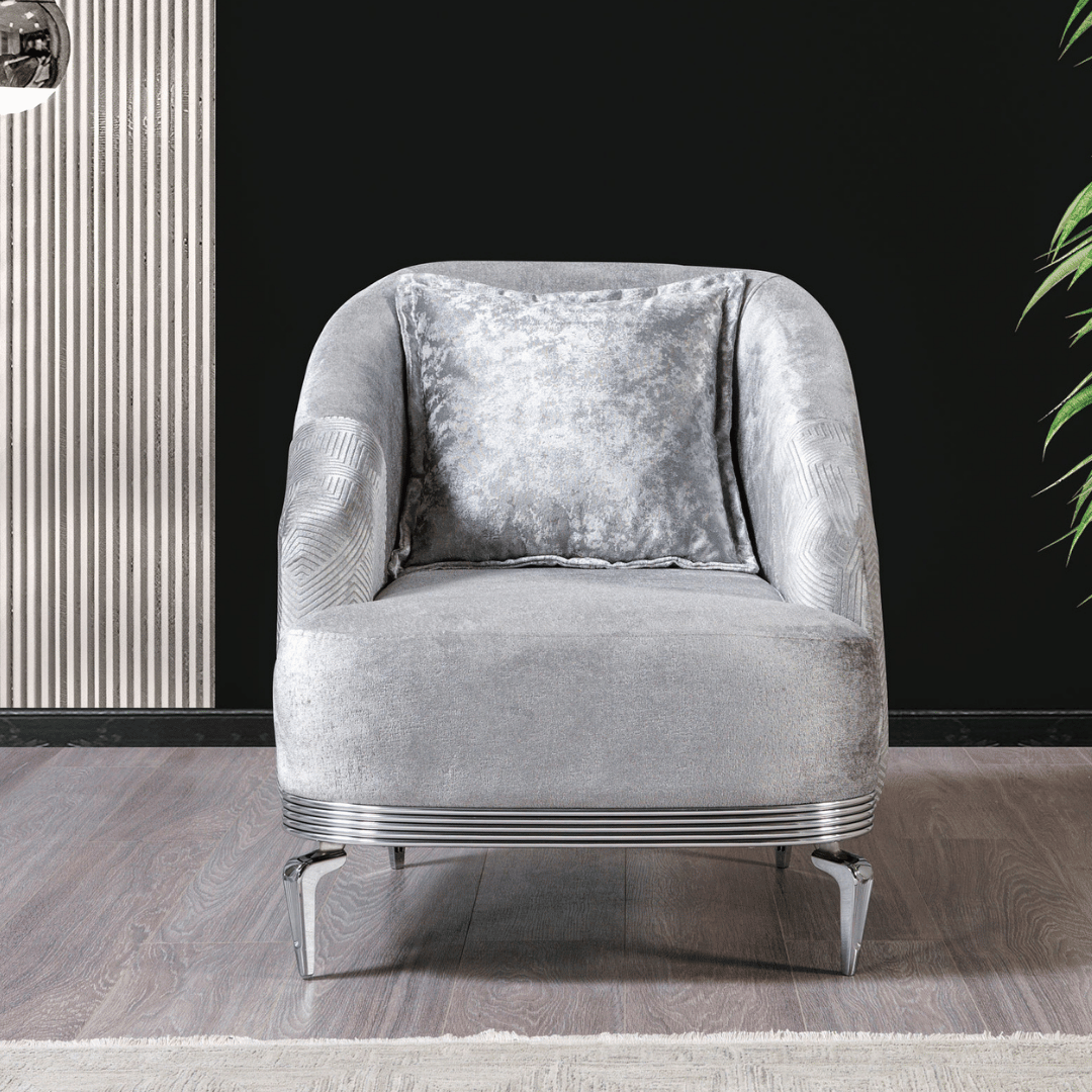 Gray armchair with a decorative pillow on a wooden floor against a black wall.