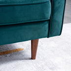 Close-up of a teal velvet upholstered chair or sofa corner with a tapered wooden leg, shown on a light gray rug.