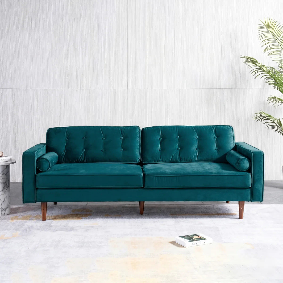 A mid-century modern two-seater sofa upholstered in deep teal velvet, featuring tufted back cushions, rolled armrests, and tapered wooden legs, set against a light gray paneled wall.
