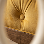 Close-up of a mustard yellow tufted velvet upholstery with a wooden base visible along the bottom edge.