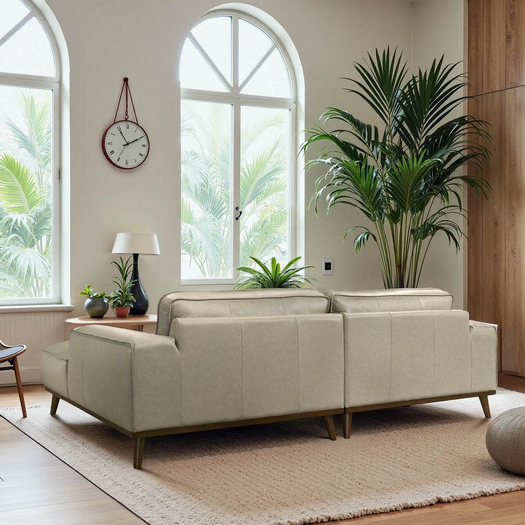 Beige sofa in a room with large windows, plants, and a clock.