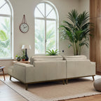 Beige sofa in a room with large windows, plants, and a clock.