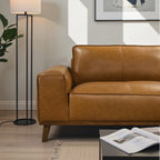 Brown leather sofa in a living room with a lamp and magazine.
