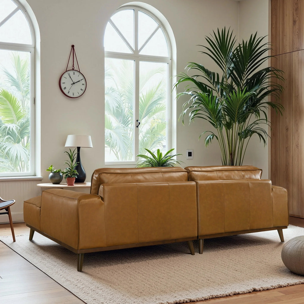 Brown leather sofa in a living room with large windows, plants, and a clock.