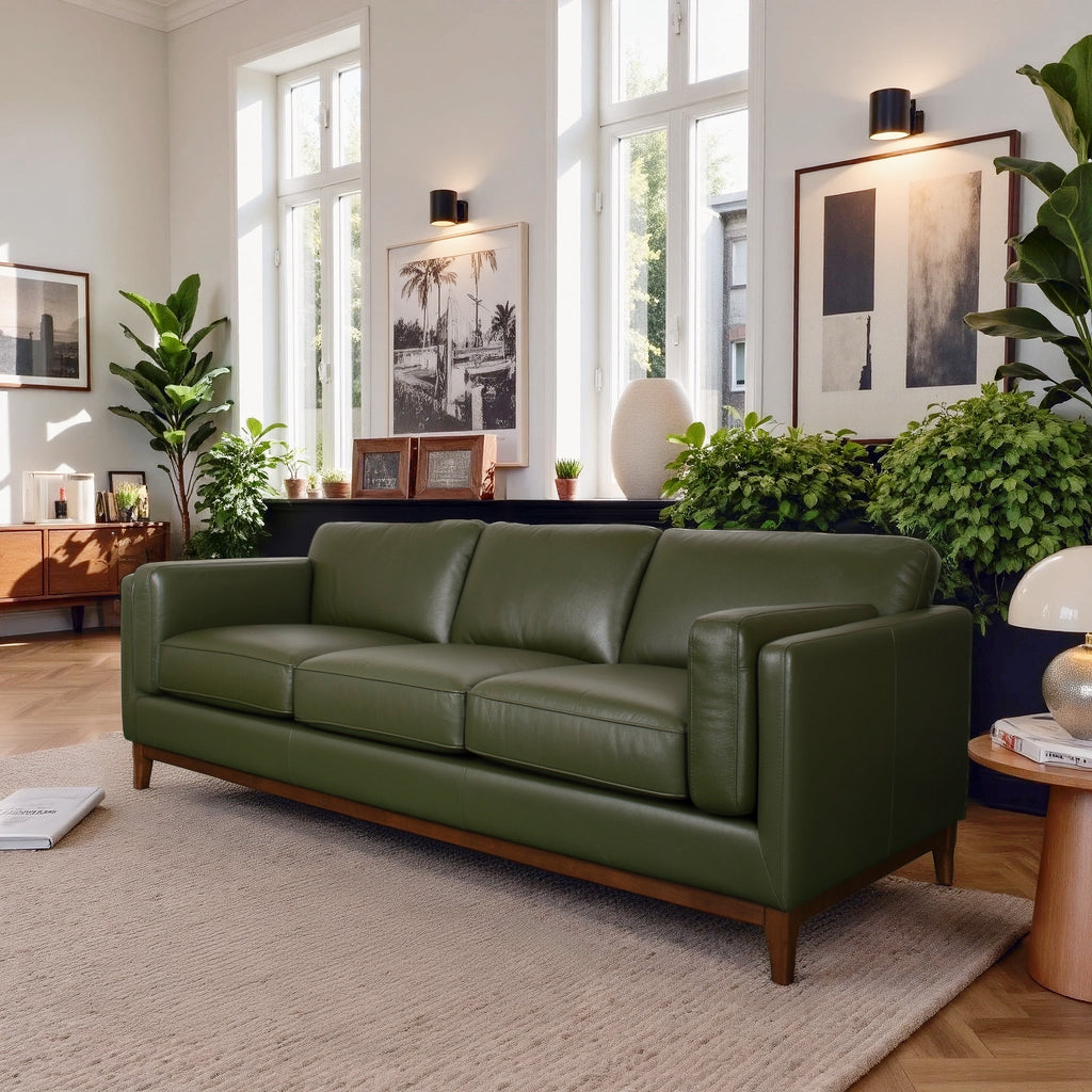 Green leather sofa in a modern living room with large windows and decorative plants.