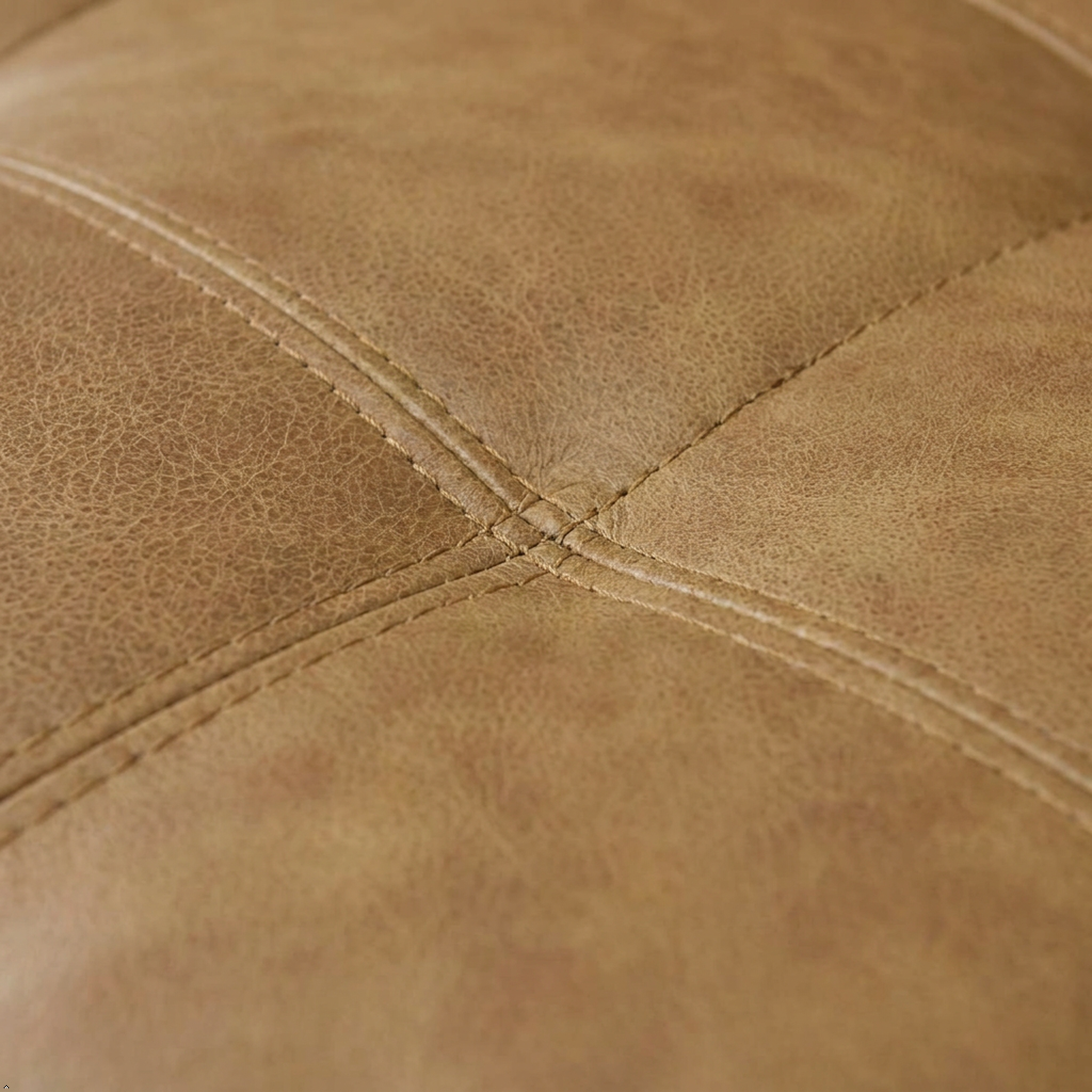 Close-up of a tan leather or faux leather upholstered surface with visible grain texture and stitched panel seams.