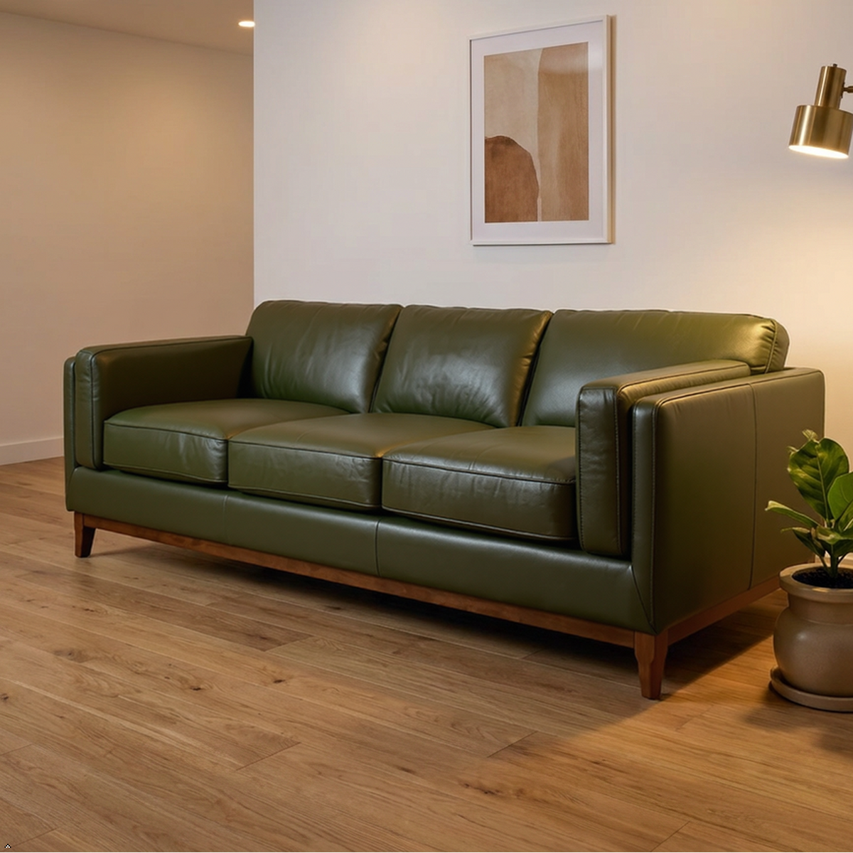 An olive green leather three-seater sofa in a modern living room setting with a wooden floor, a brass floor lamp, a potted plant, and framed wall art.
