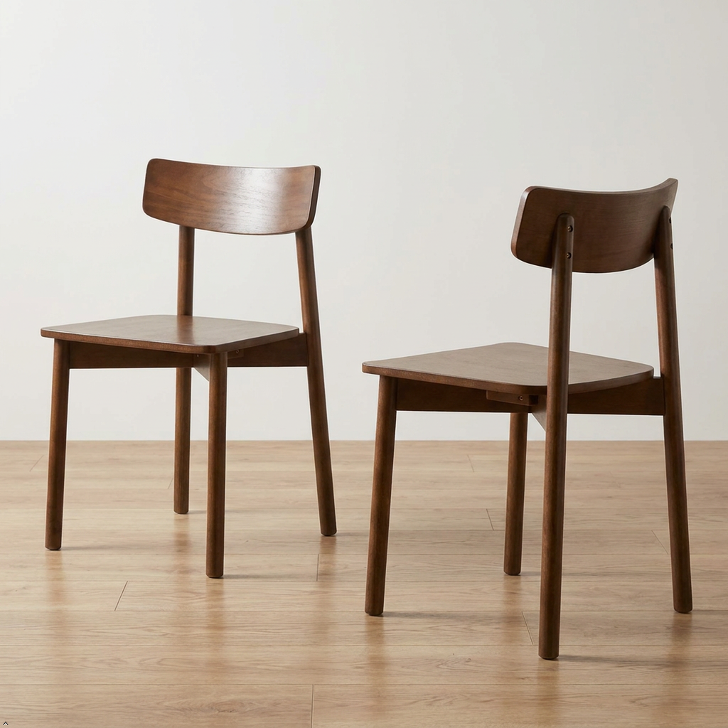 Two wooden dining chairs with a warm medium-brown finish, shown from different angles on a light wood floor against a plain off-white wall.